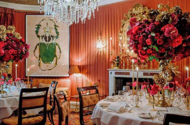 Room set with circular tables for an event with decor including a large red rose display and a chandelier