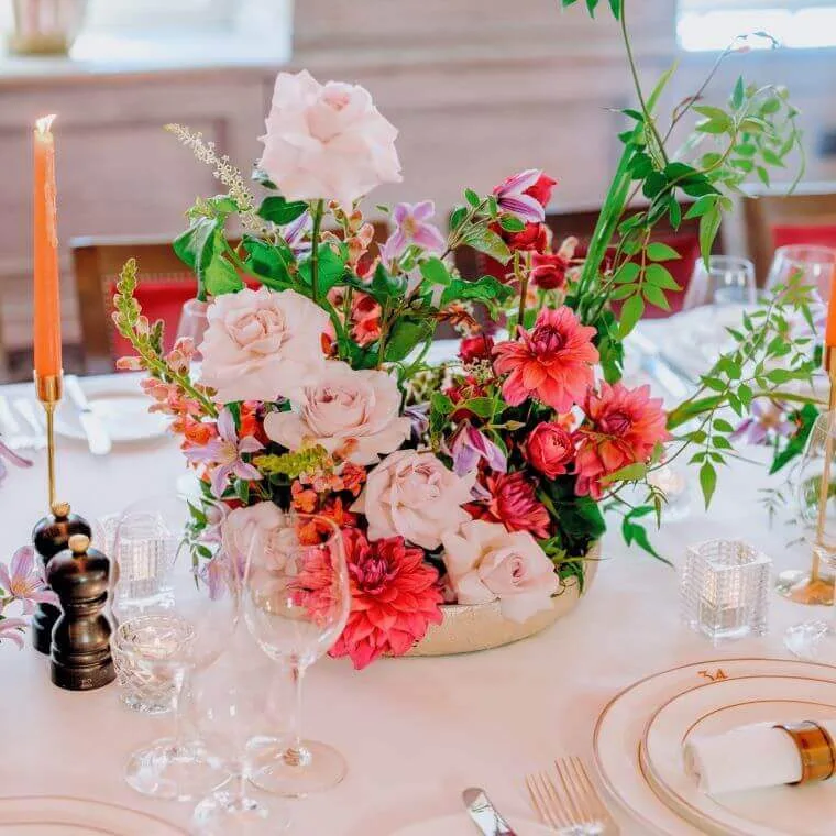 Pink and white flowers in a table centrepiece accompanied by candles and a table setting