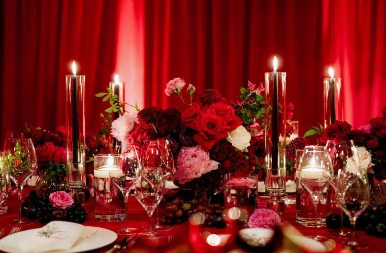 Opulent florals with deep red and pink flowers and red candles against a backdrop of red curtains