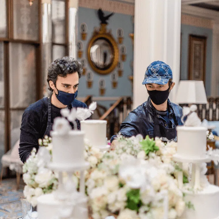 Two men from blooming haus working on a display for a wedding featuring white wedding cake sections