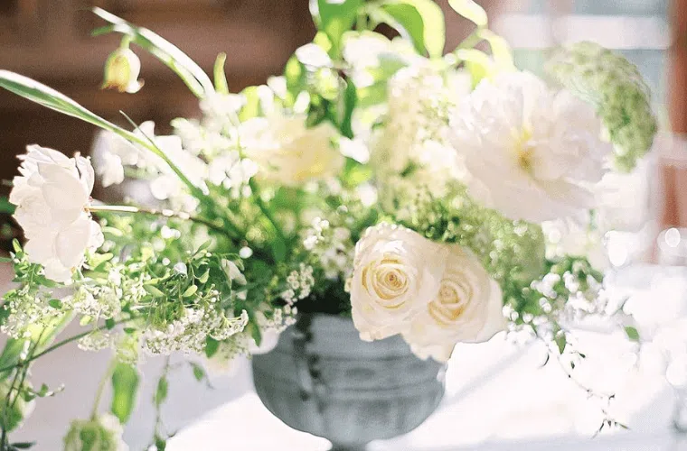 a table top display with white roses and green foliage