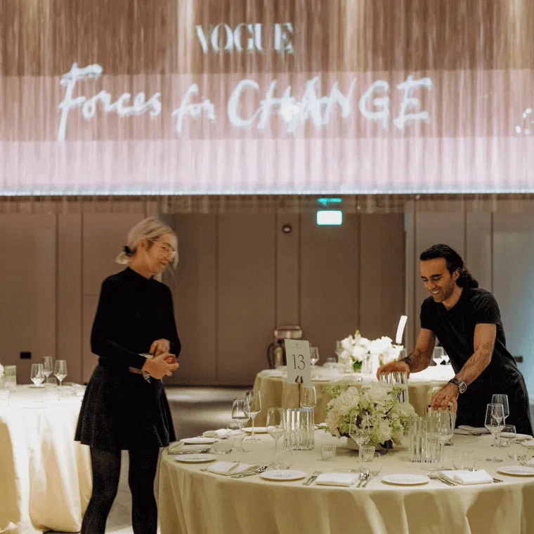 Male and female setting floral centrepieces on a round table with a white covering