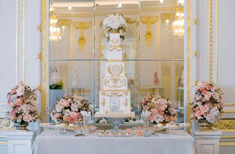A gold and white wedding cake accompanied by four floral centrepieces
