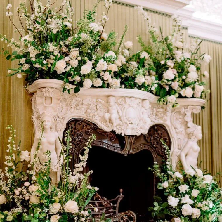 White and green floral displays around a fireplace and mantlepiece