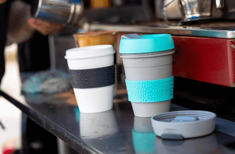 How can my business help fight climate change in 2025? 11 Two reusable cups on a metal shelf with a blurred background