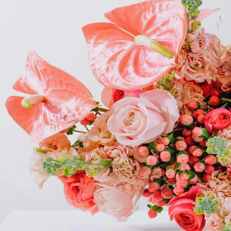 A bouquet of flowers in different shades of pink including pink avalanche roses and peach anthuriums