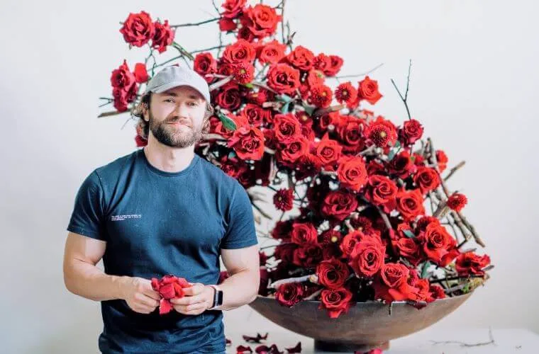 Master florist michal standing beside his sustainable design created with red roses