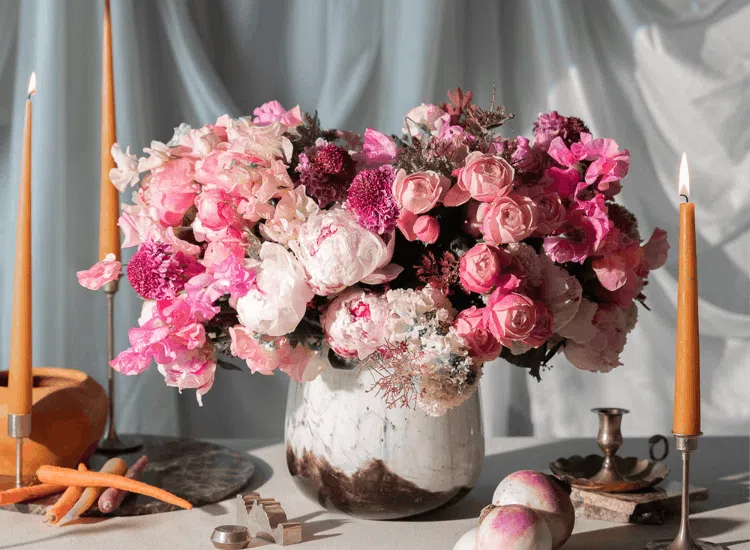 Sweet pea: blooming haus' flower of the year for 2026 22 A marble vase holding a large bouquet of pink and white sweet pea flowers on a table with lit orange taper candles and a brass tray