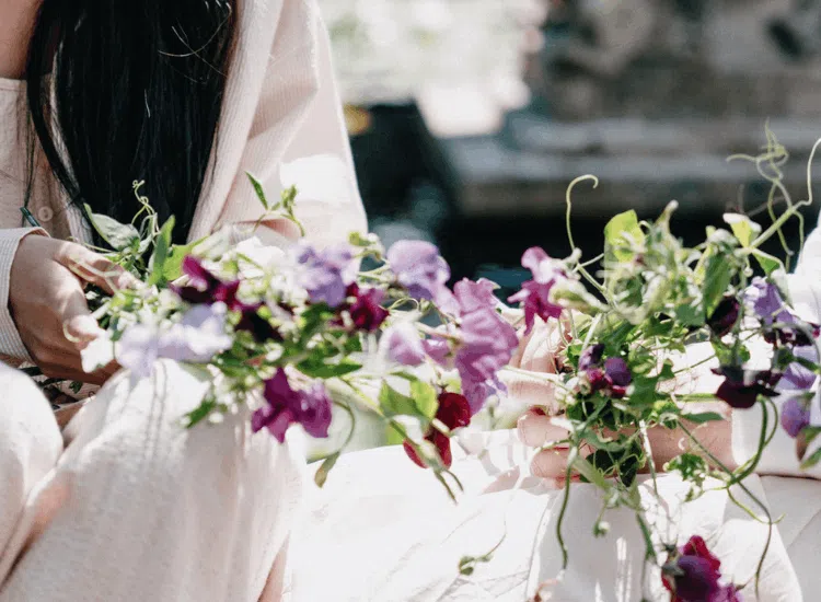 Sweet pea: blooming haus' flower of the year for 2026 14 Two people arranging bunches of sweet pea and violet flowers in natural sunlight